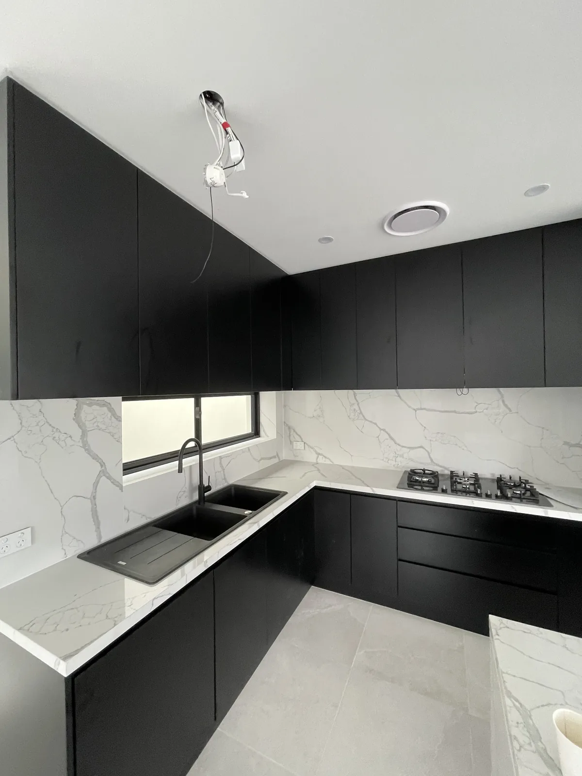 Black matt kitchen corner with a Calacatta Maximus full-height stone splashback, black sink and gas cooktop