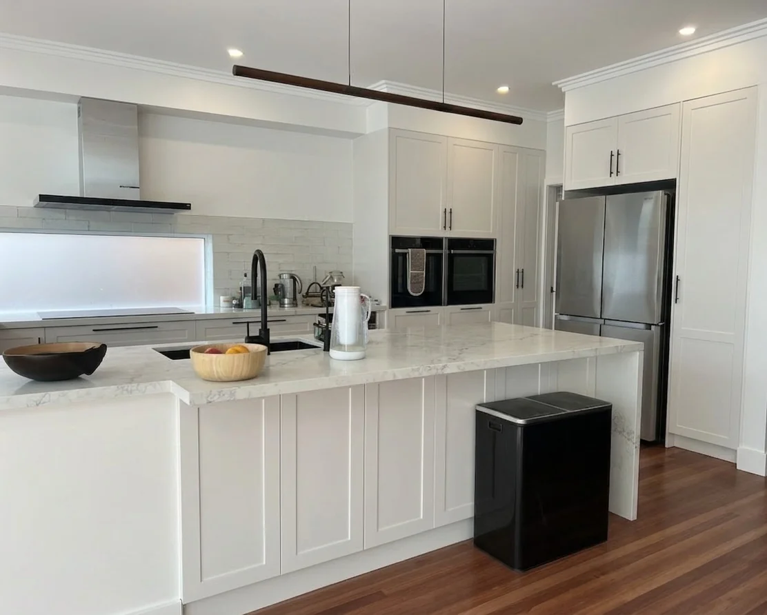 Kitchen island with Caesarstone benchtop, stacked ovens and integrated fridge in background