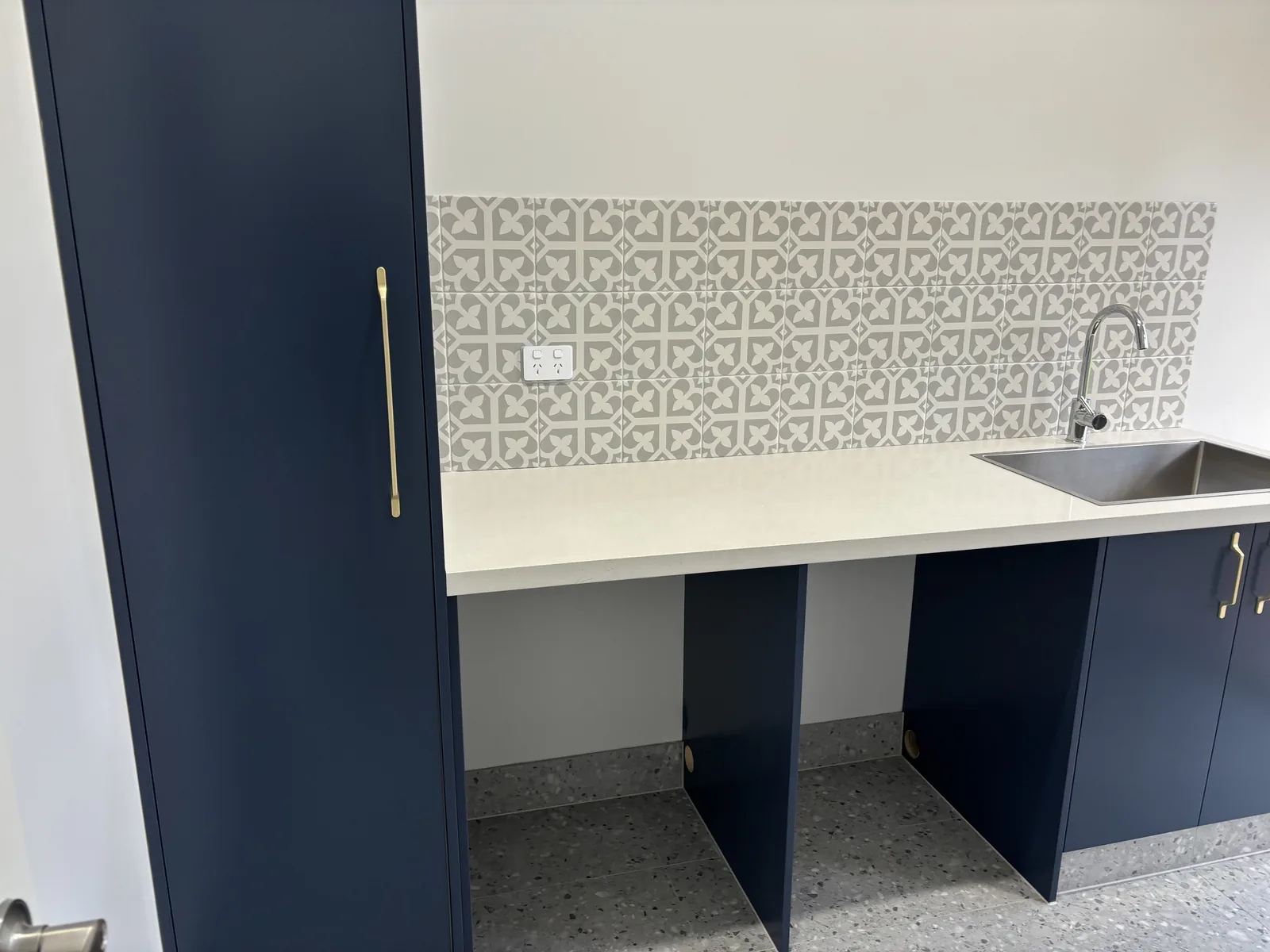 Navy laundry joinery with a stainless tub, brass handles and a patterned tile splashback