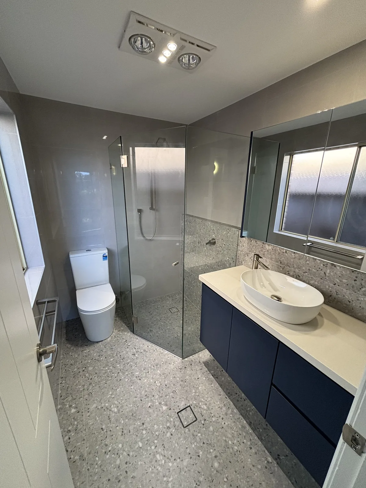 Navy floating vanity with a mirrored shaving cabinet beside a frameless corner shower