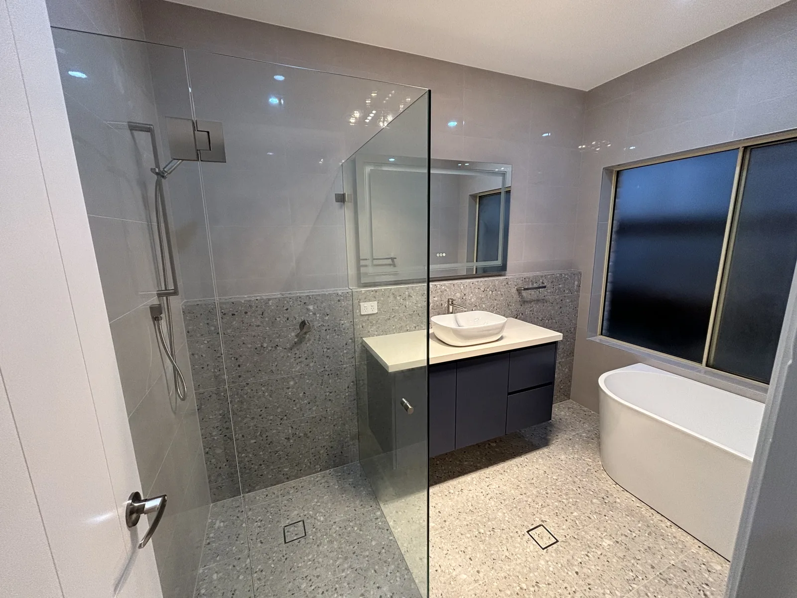 Bathroom with a navy floating vanity, freestanding bath and frameless walk-in shower