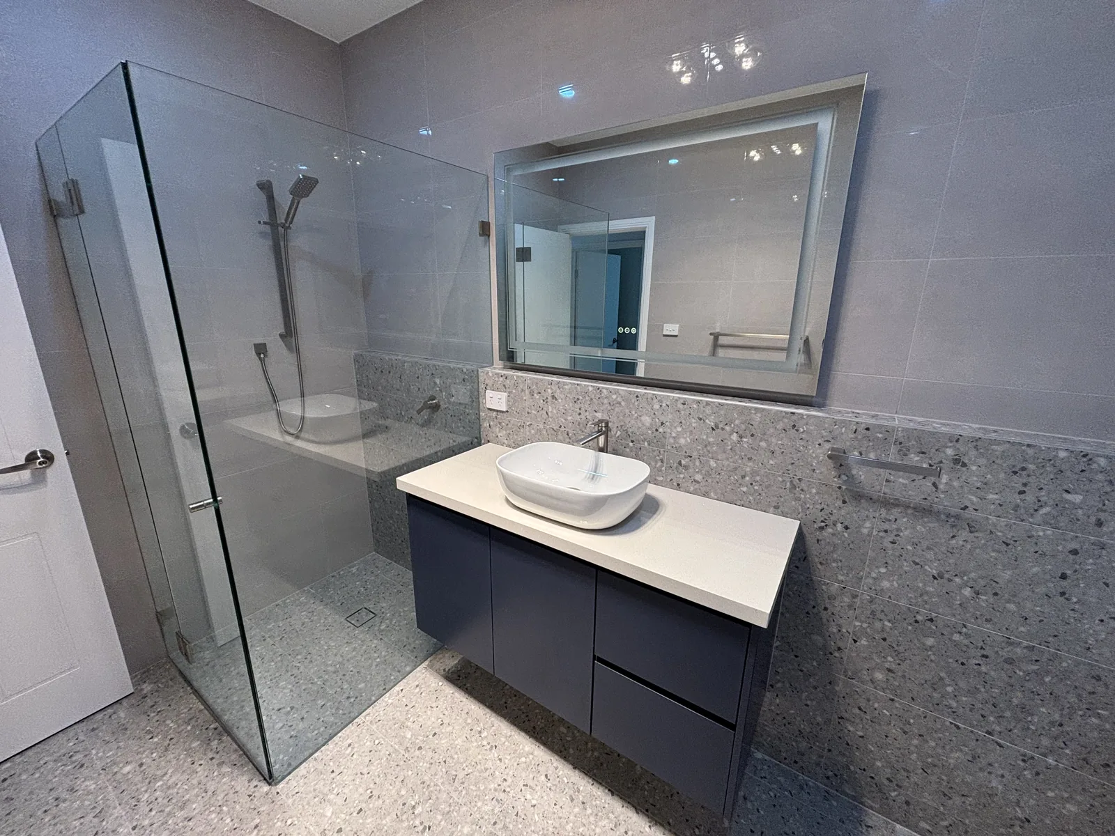 Frameless corner shower with a built-in bench beside a navy floating vanity